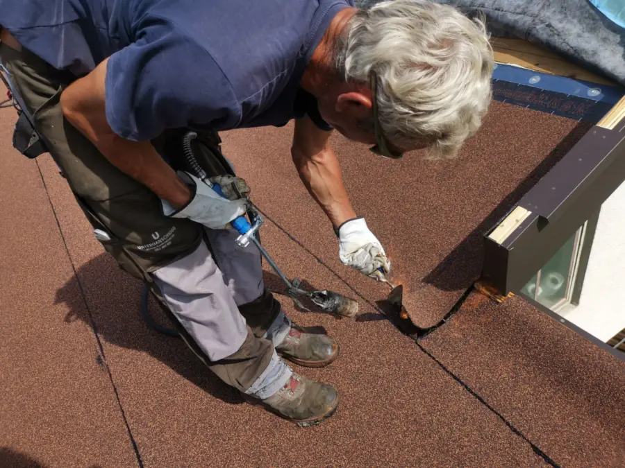 Dakdekker brandt een gegranuleerde bitumen baan vast langs de opstand van een dakraam