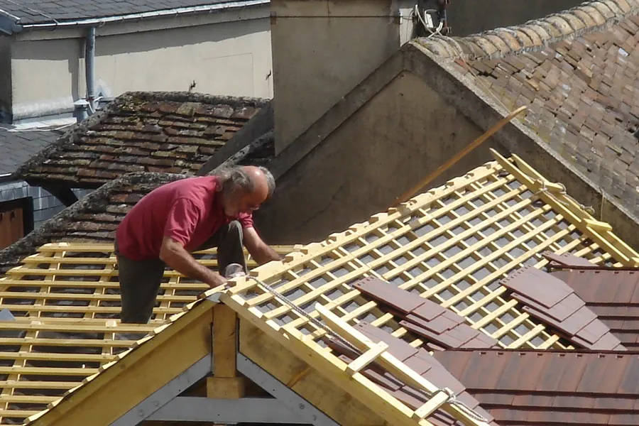 Dakdekker werkt aan een nieuwe kapconstructie met blanke panlatten en de eerste dakpannen, opbouw van een dakkapel
