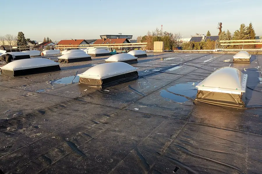 Plat dak met bitumen dakbedekking, lichtkoepels en plassen water die na regen blijven staan