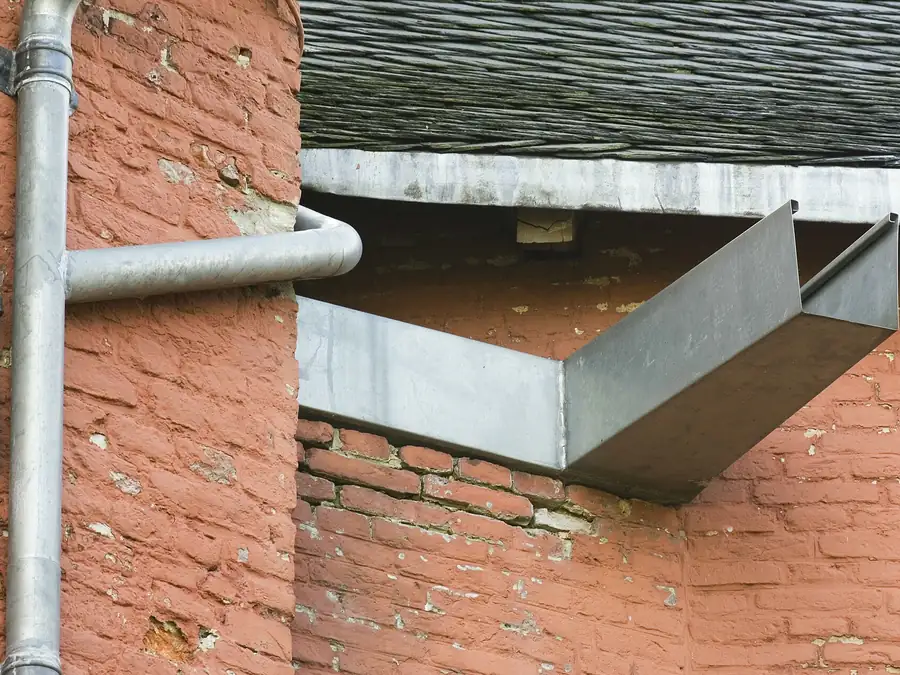 Uitloop van een zinken bakgoot met regenpijp tegen baksteen, illustratie bij dakgoten in Amsterdam
